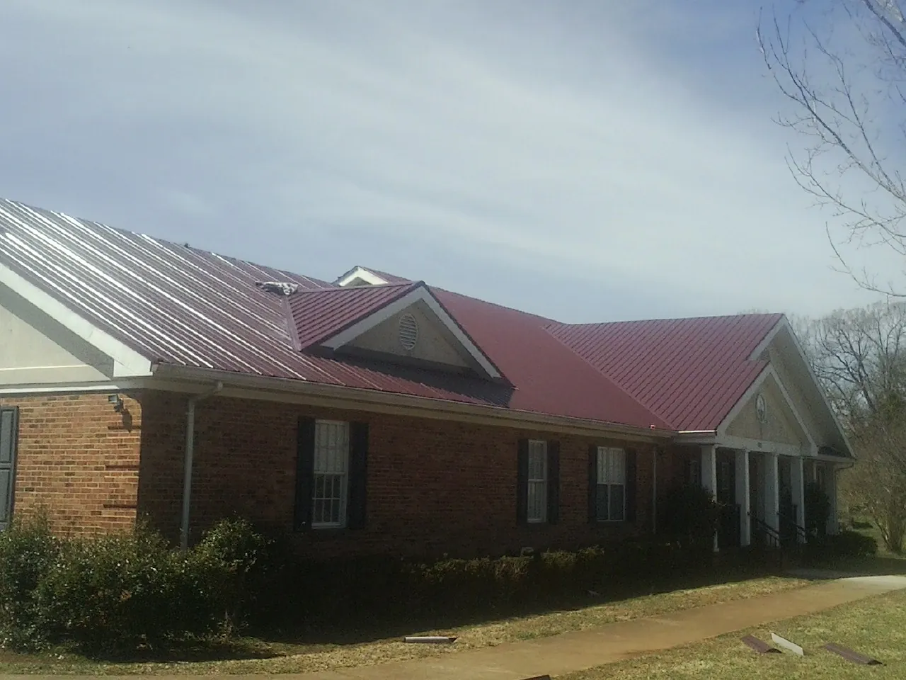 Red metal roof with gabled entries on a long brick building, from a Hail Damage Roof Repair job in Fort Leavenworth