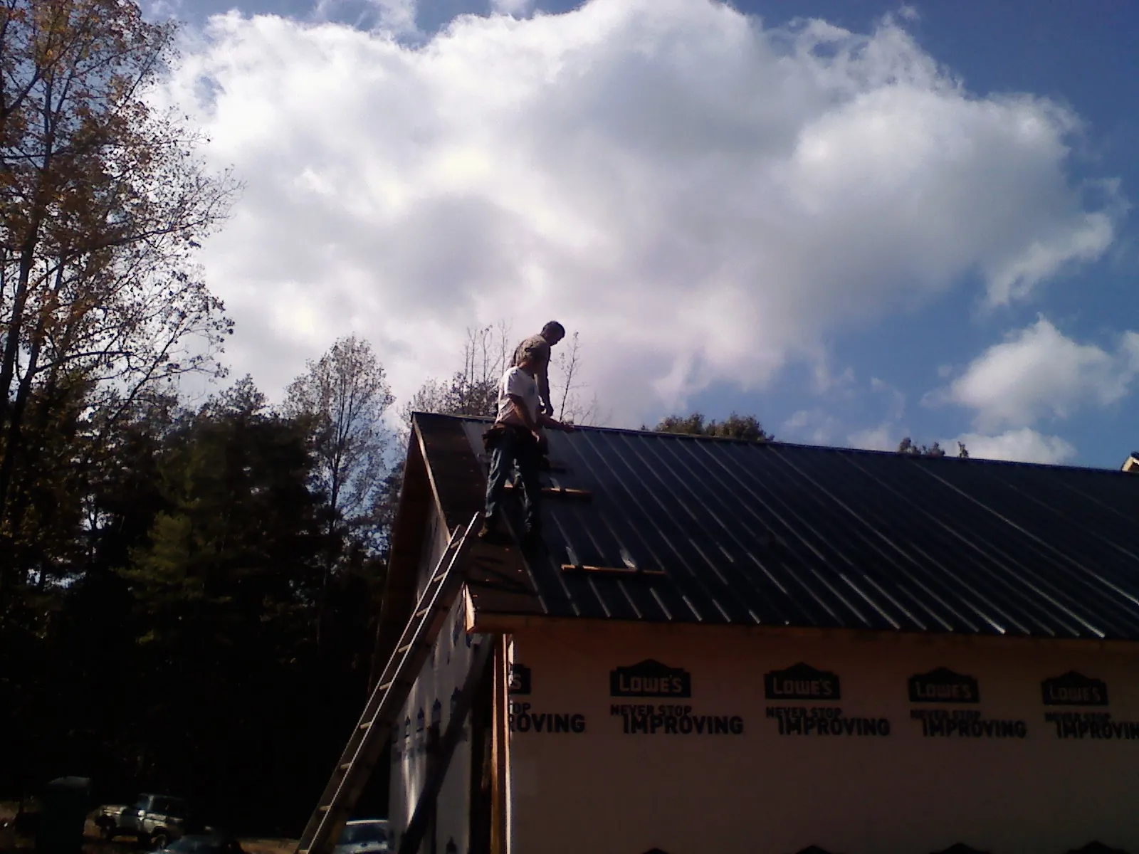 Roofer fastening dark metal panels high against a cloudy sky, from a Roof Inspection job in Fort Leavenworth
