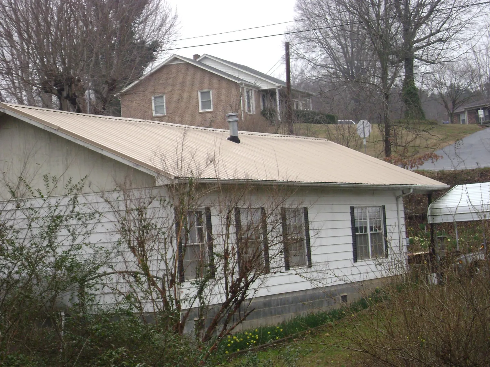 Tan metal roof on a white sided house set into a hillside — Commercial Roofing by Roofing Brothers in Fort Leavenworth